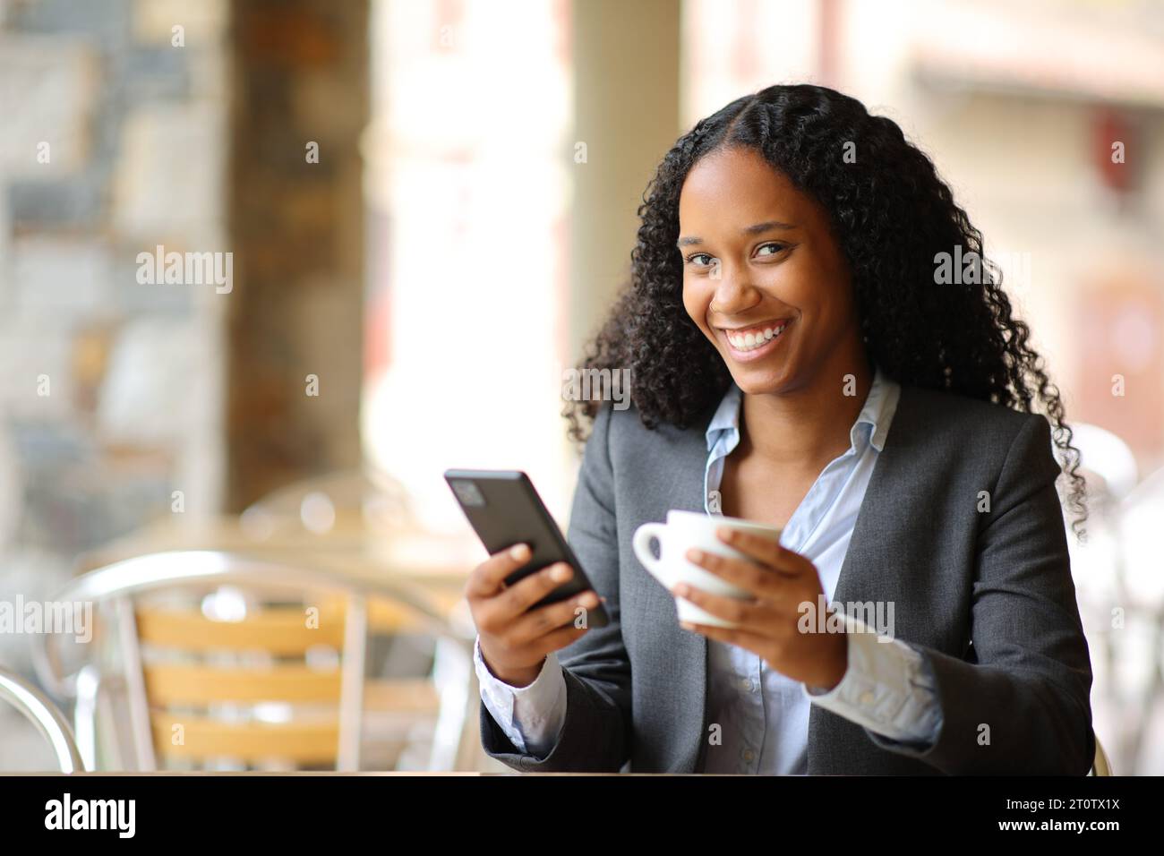 Glücklicher schwarzer Manager mit Smartphone und Kaffeetasse, der in einem Restaurant in die Kamera blickt Stockfoto