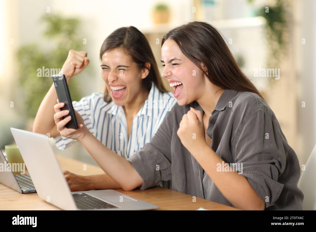 Begeisterte Mitbewohner, die am Telefon gute Nachrichten lesen, feiern den Erfolg zu Hause Stockfoto