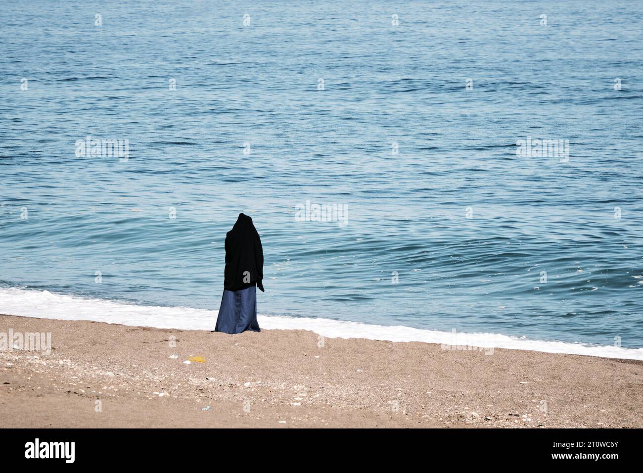 Eine Frau, die einen Jilbab trägt und das Meer am Strand beobachtet. An einem bewölkten Tag. Stockfoto