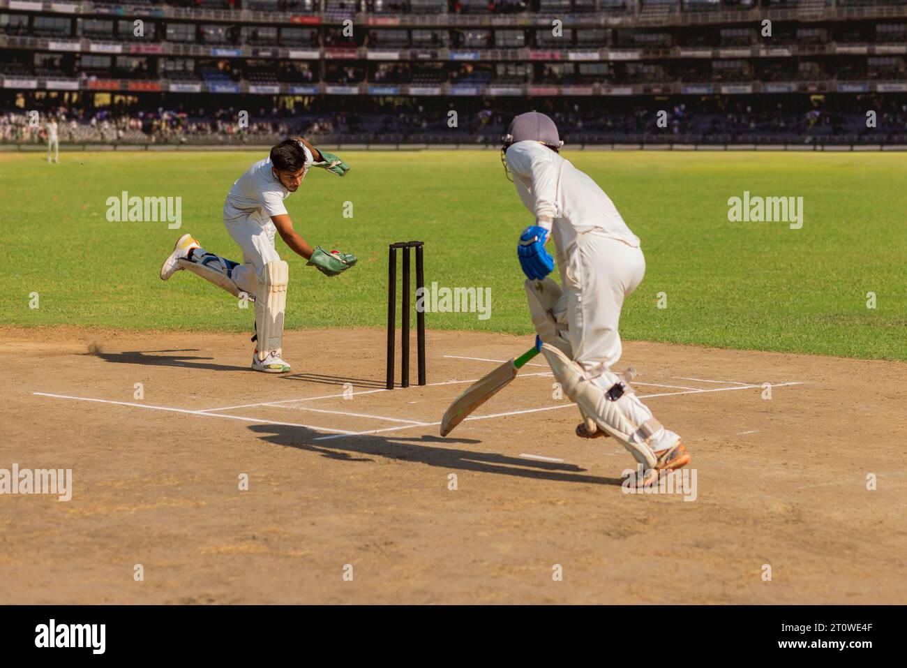 Batsman läuft, als der Wicket Keeper versucht, ihn während eines Cricketspiels auszuschalten Stockfoto