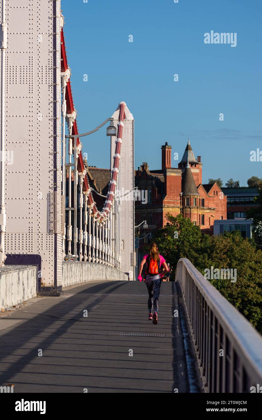 Einsame Joggerin, die früh am Morgen über die Chelsea Bridge läuft, Richtung Battersea. Trage Laufausrüstung für kaltes Wetter Stockfoto