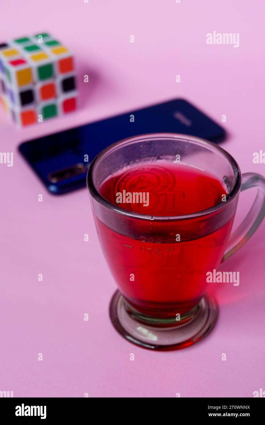 Foto von rotem Getränk, blauem Smartphone und Rubik auf rosa Hintergrund Stockfoto