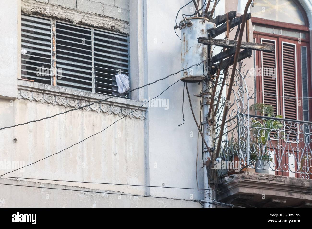 Ein Stromtransformator ist an einer alten Holzkonstruktion in einem Metallmast befestigt. Die Wand und die Fenster im Gebäude sind verwittert und alt. Stockfoto