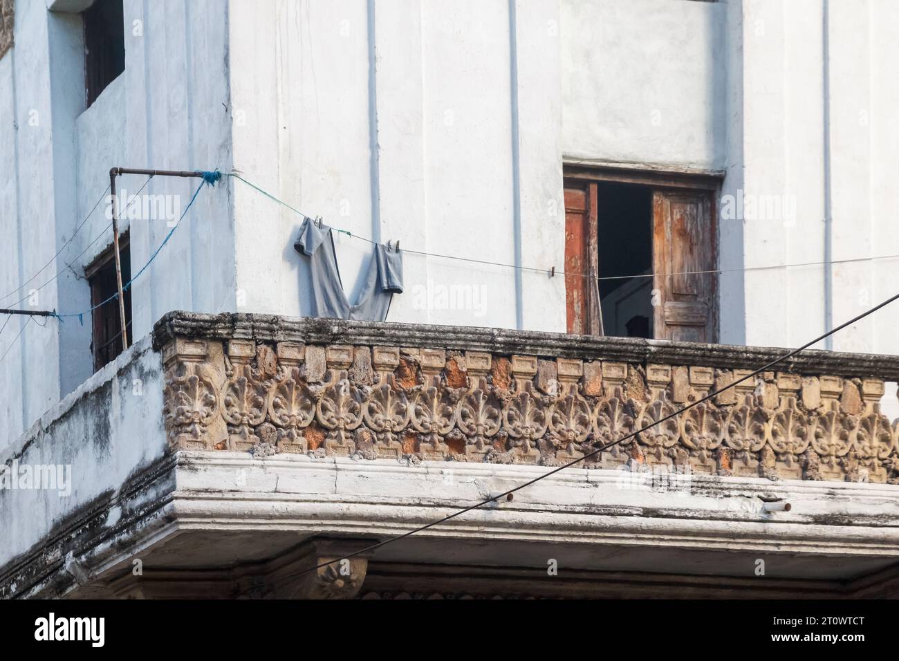 Eine Hose, die in einer Wäscheleine trocknet. Das Geländer des Balkons ist mit Ziegeln verstärkt. Das Gebäude weist einige Schäden an den Holztüren auf. Stockfoto