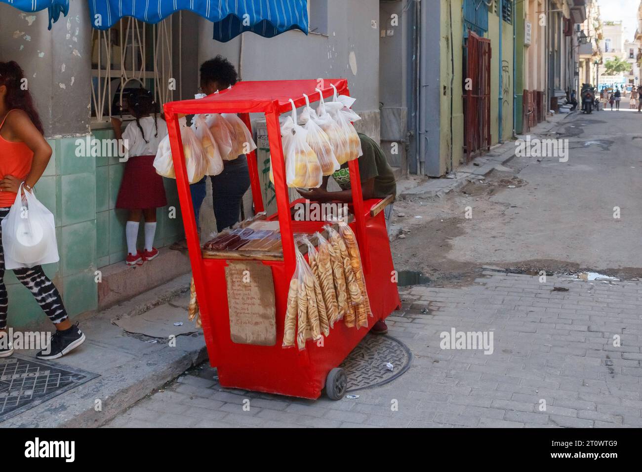 Ein Wagen mit Crackern und Brot auf einer kaputten Kopfsteinpflasterstraße in Old Havanna. Kubanische Leute in ihrer Routine gehen durch die Szene. Stockfoto