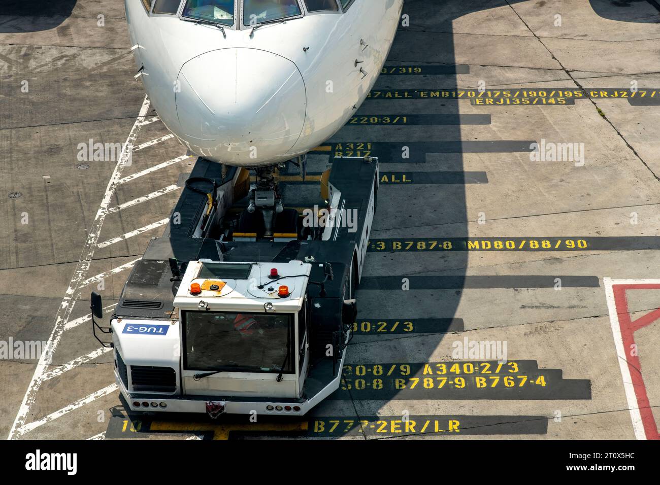 Hochwinkelansicht von Flugzeugen, die an der Jetbrücke geparkt sind, auf gelbem Flughafentor auf dem Asphalt vor dem Gate mit Schubtraktor oder Flughafenschlepper i Stockfoto
