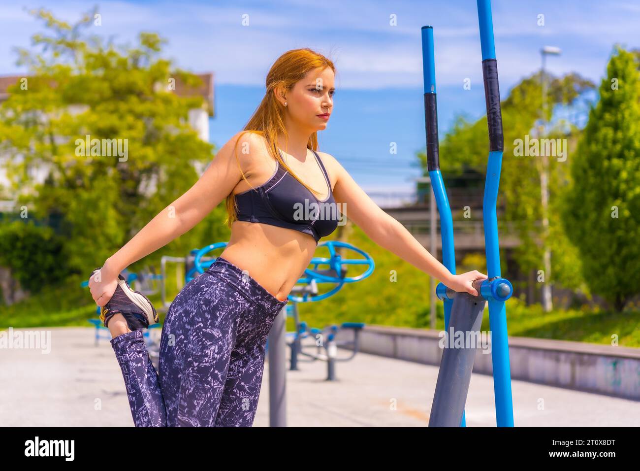 Rothaarige Frau mit lila Leggings und schwarzem Overall, die auf Maschinen trainiert, dehnt, Sport in der Stadt macht Stockfoto