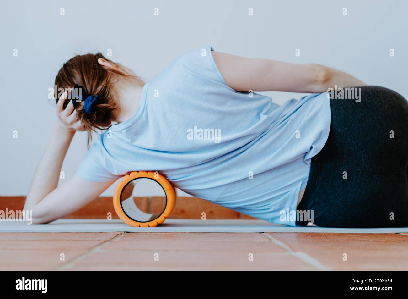Frau, die die untere Achselhöhle auf der Massageschaumrolle rollt, um die Spannung in den Seitenkörpermuskeln zu lösen Stockfoto
