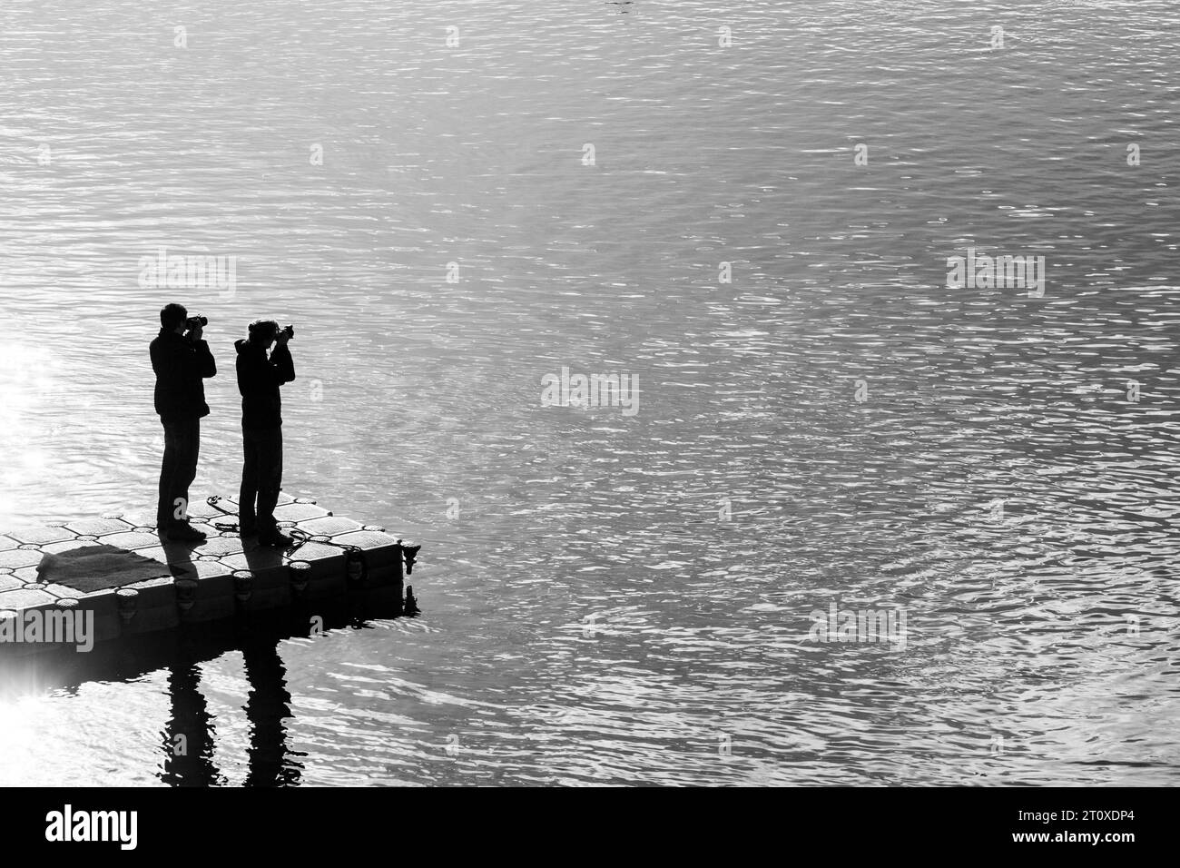 Silhouette von zwei Personen am Dock, die mit ihren Kameras auf ein großes Gewässer, Jokulsarlon Glacier Lagoon, Island, zielen Stockfoto