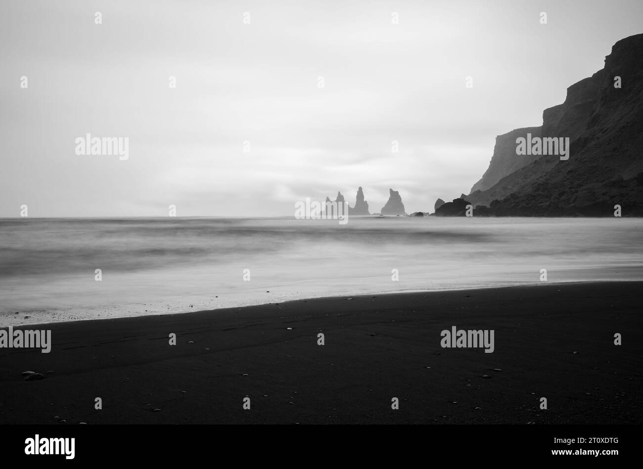 Schwarzer Sandstrand mit Reynisdrangar Basaltmeerstapel und Klippen im Hintergrund an nebelhaltigen Tagen, in der Nähe von Vik i Myrdal, Island Stockfoto