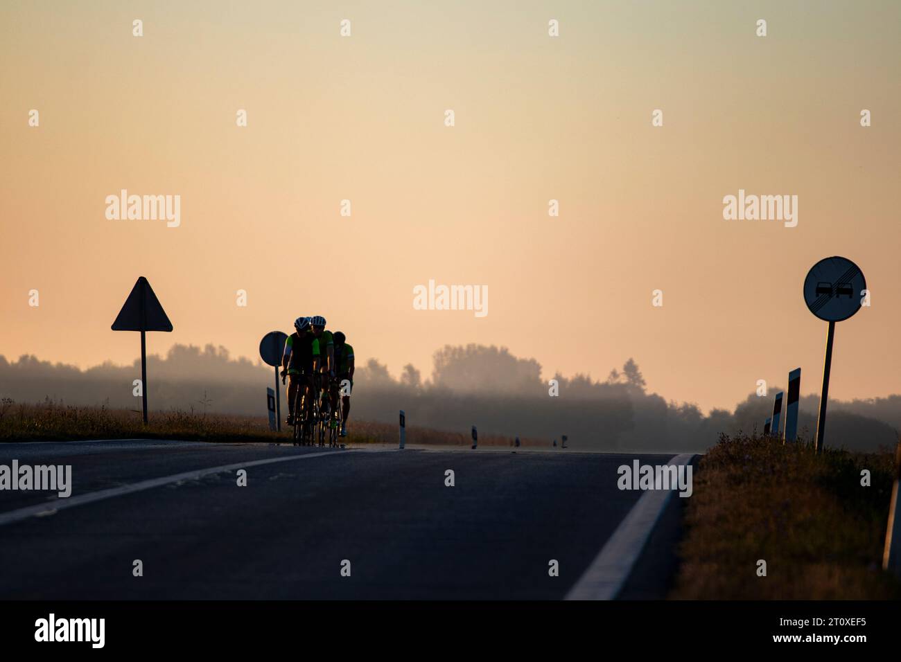 Gruppe von Radfahrern am Morgen Sonnenaufgang auf der Asphaltstraße mit Schildern auf beiden Seiten der Straße Stockfoto