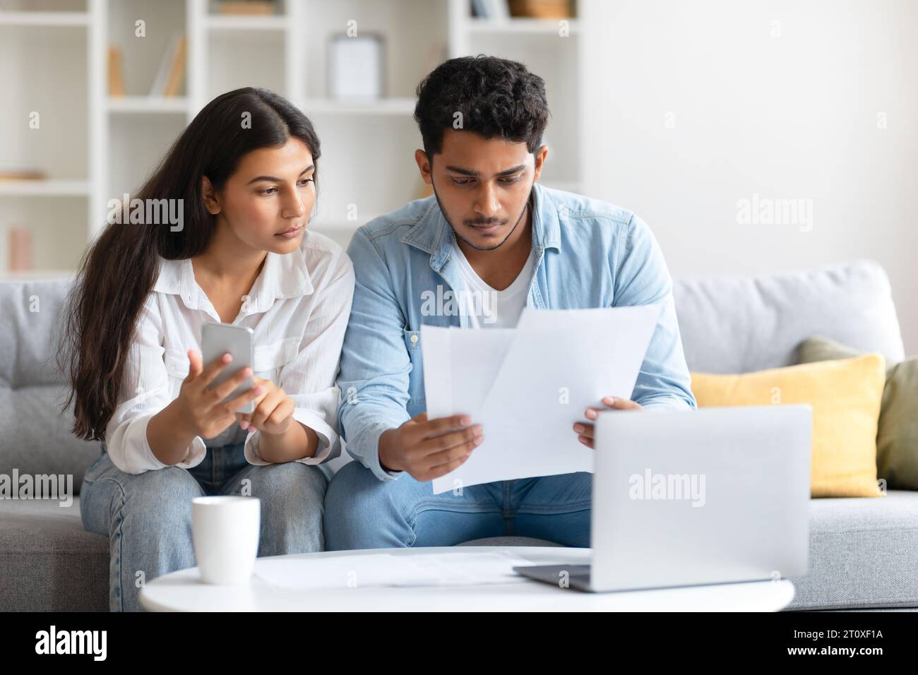 Indisches Paar konzentrierte sich auf Rechnungen und benutzte Handy, saß auf dem Sofa Stockfoto