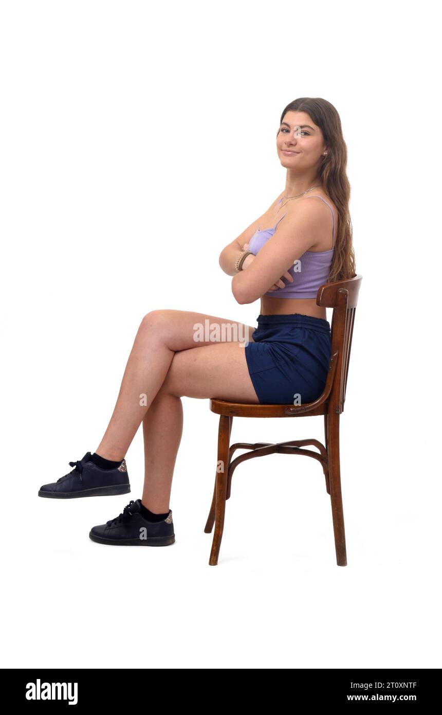 Seitenansicht eines jungen Mädchens, das auf einem Stuhl sitzt und in die Kamera blickt, mit den Beinen und den Armen auf weißem Hintergrund Stockfoto