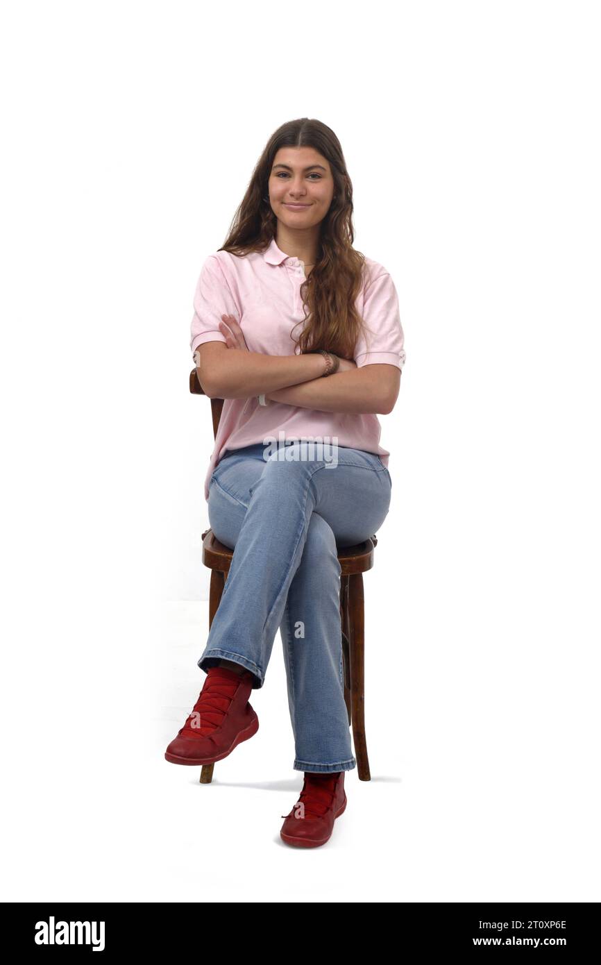 Vorderansicht eines jungen Mädchens, das auf einem Stuhl sitzt, mit überkreuzten Armen und Blick auf die Kamera auf weißem Hintergrund Stockfoto