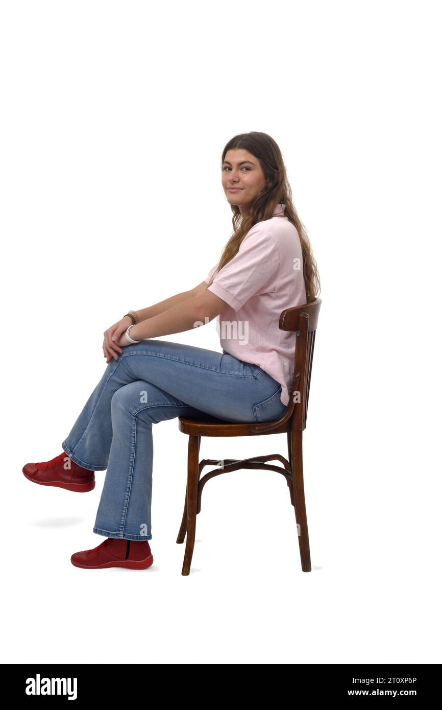 Seitenansicht eines jungen Mädchens, das auf einem Stuhl sitzt und in die Kamera auf weißem Hintergrund blickt Stockfoto