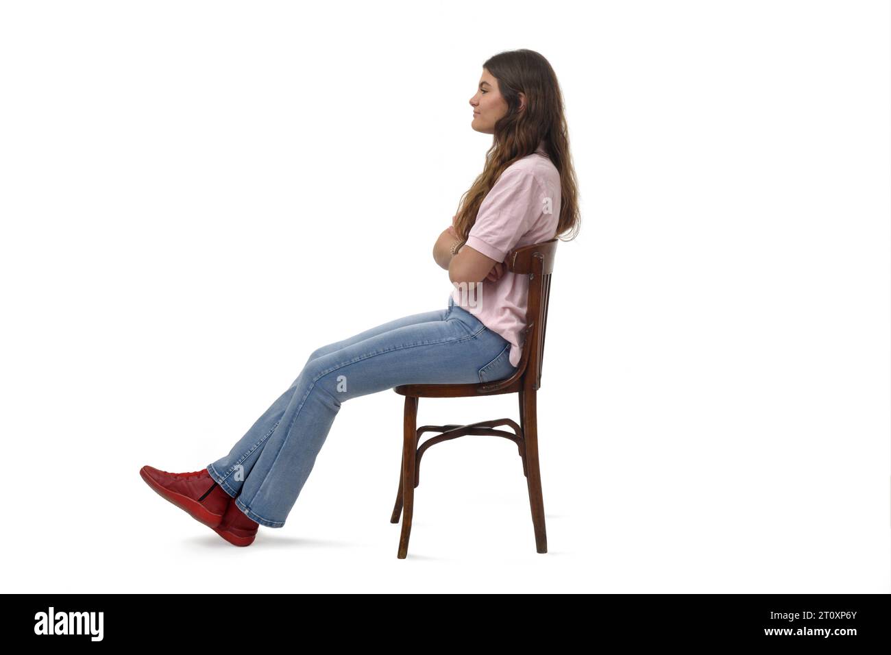 Seitenansicht eines jungen Mädchens, das auf einem Stuhl sitzt, mit überkreuzten Armen auf weißem Hintergrund Stockfoto