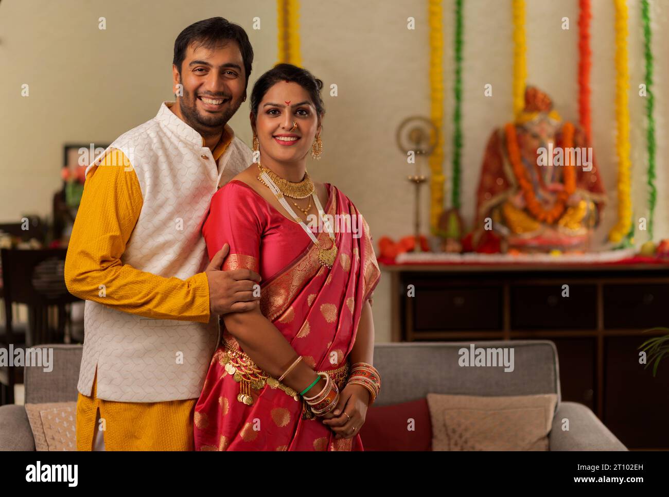 Glückliches, junges Paar in traditioneller Kleidung, das zu Hause bei Ganesh Chaturthi zusammen steht Stockfoto