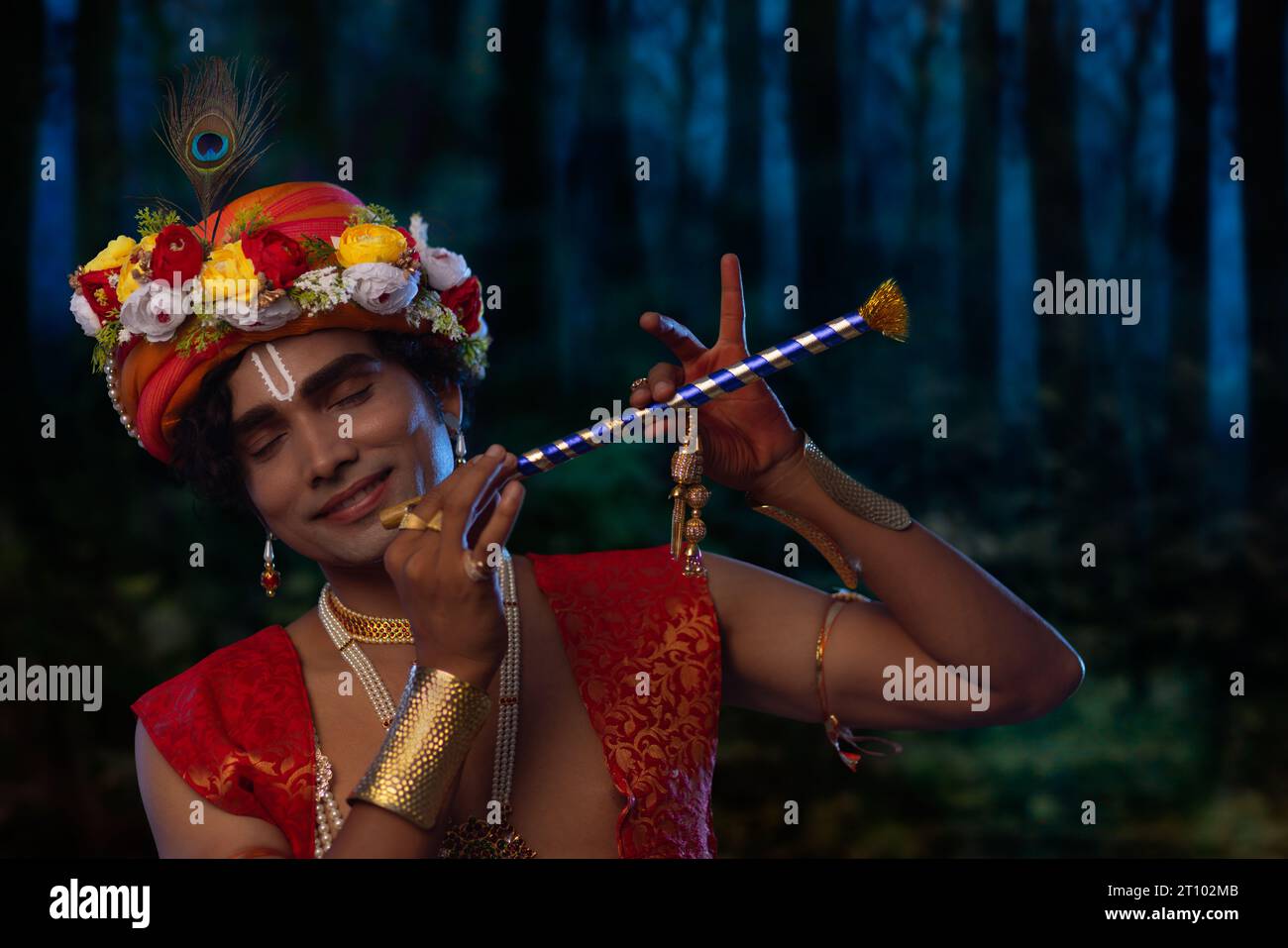 Porträt eines jungen Mannes, der als Lord Krishna verkleidet ist und Flöte aus Anlass von Janmashtami spielt Stockfoto