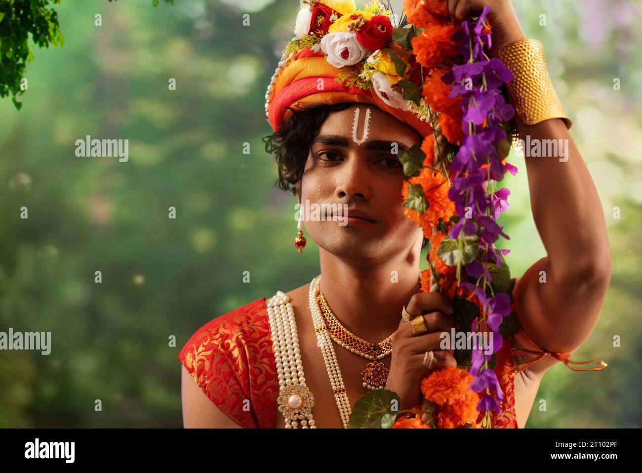 Porträt eines jungen Mannes, der als Lord Krishna verkleidet ist und anlässlich des Janmashtami auf einer Schaukel sitzt Stockfoto
