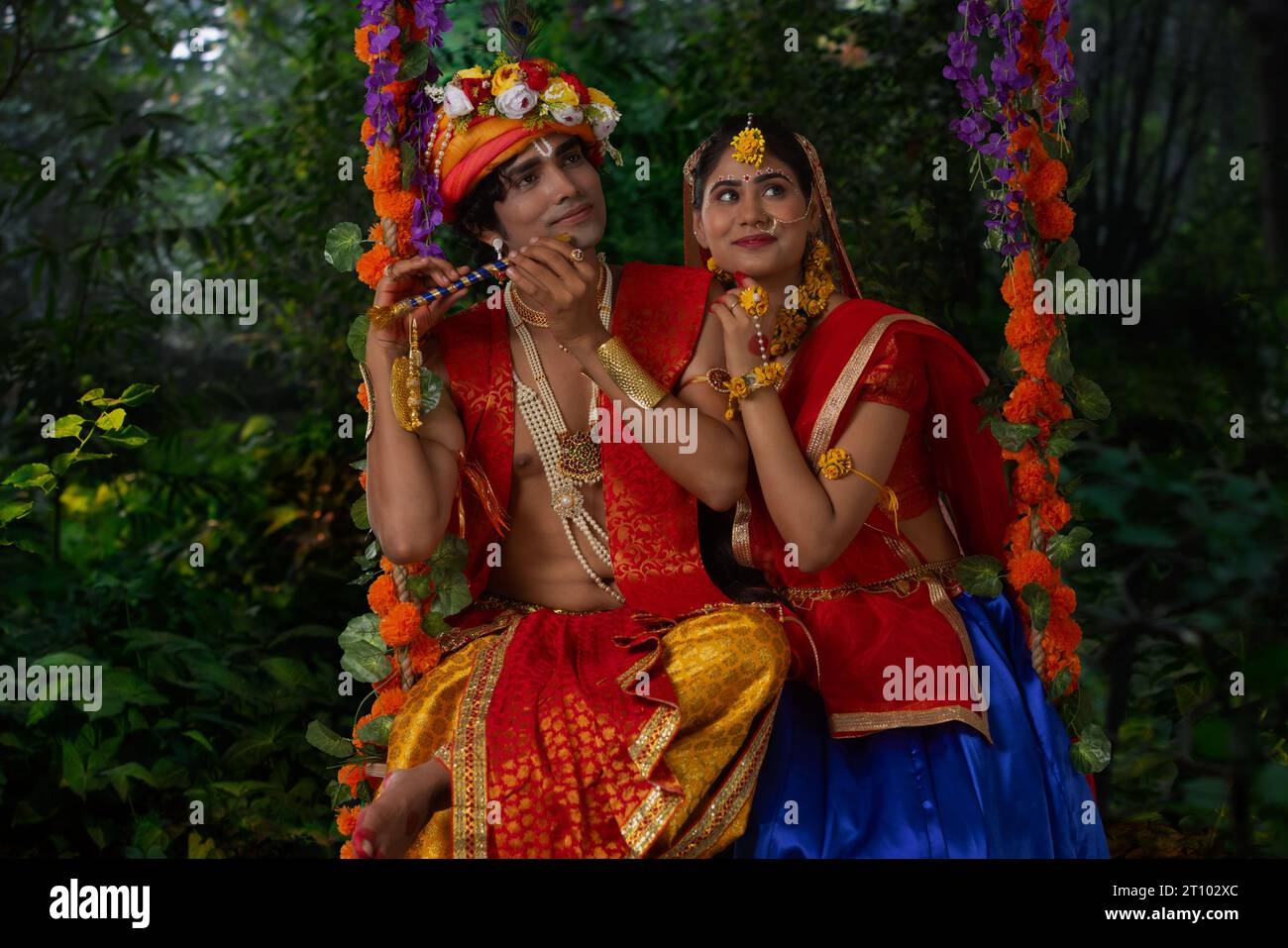Junger Mann und Frau verkleidet als Radha und Krishna und sitzen zusammen auf einer Schaukel anlässlich von Janmashtami Stockfoto