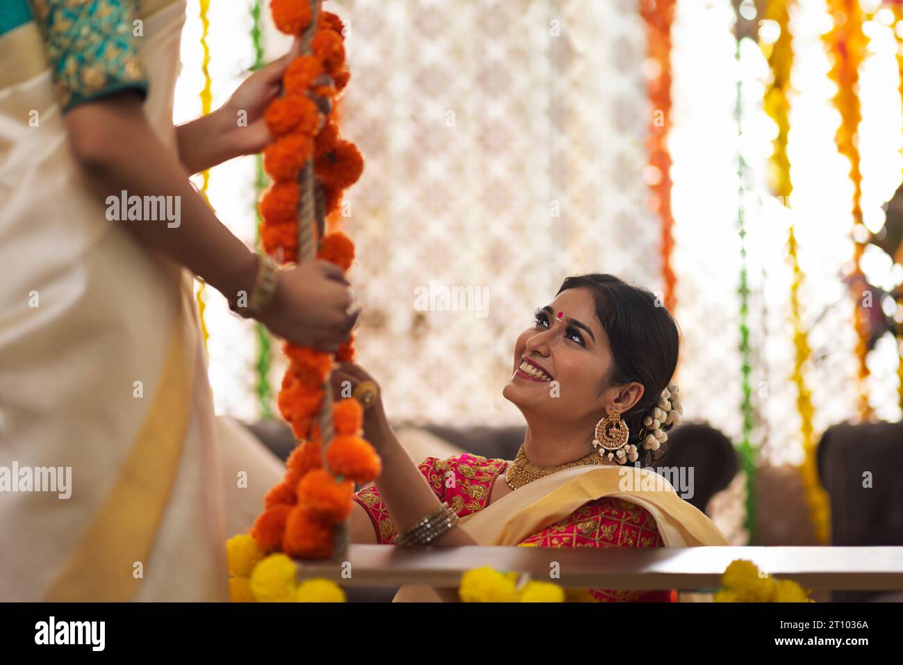 Frau in weißem Saree, die eine Schaukel mit Blumengirlande dekoriert, um Onam zu feiern Stockfoto