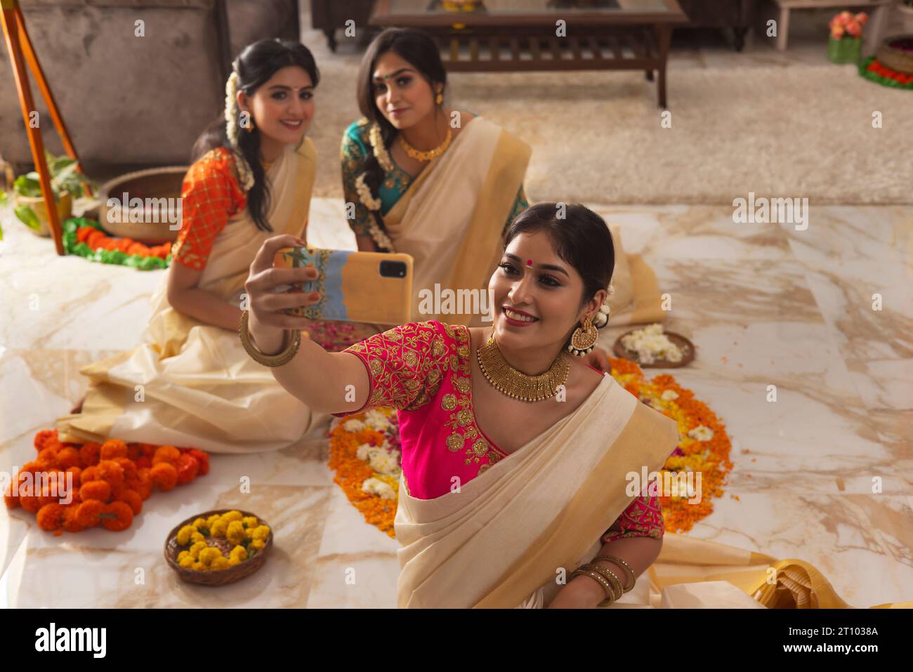 Südindische Frauen machen Selfie, während sie bei der Blumendekoration sitzen, anlässlich von Onam Stockfoto