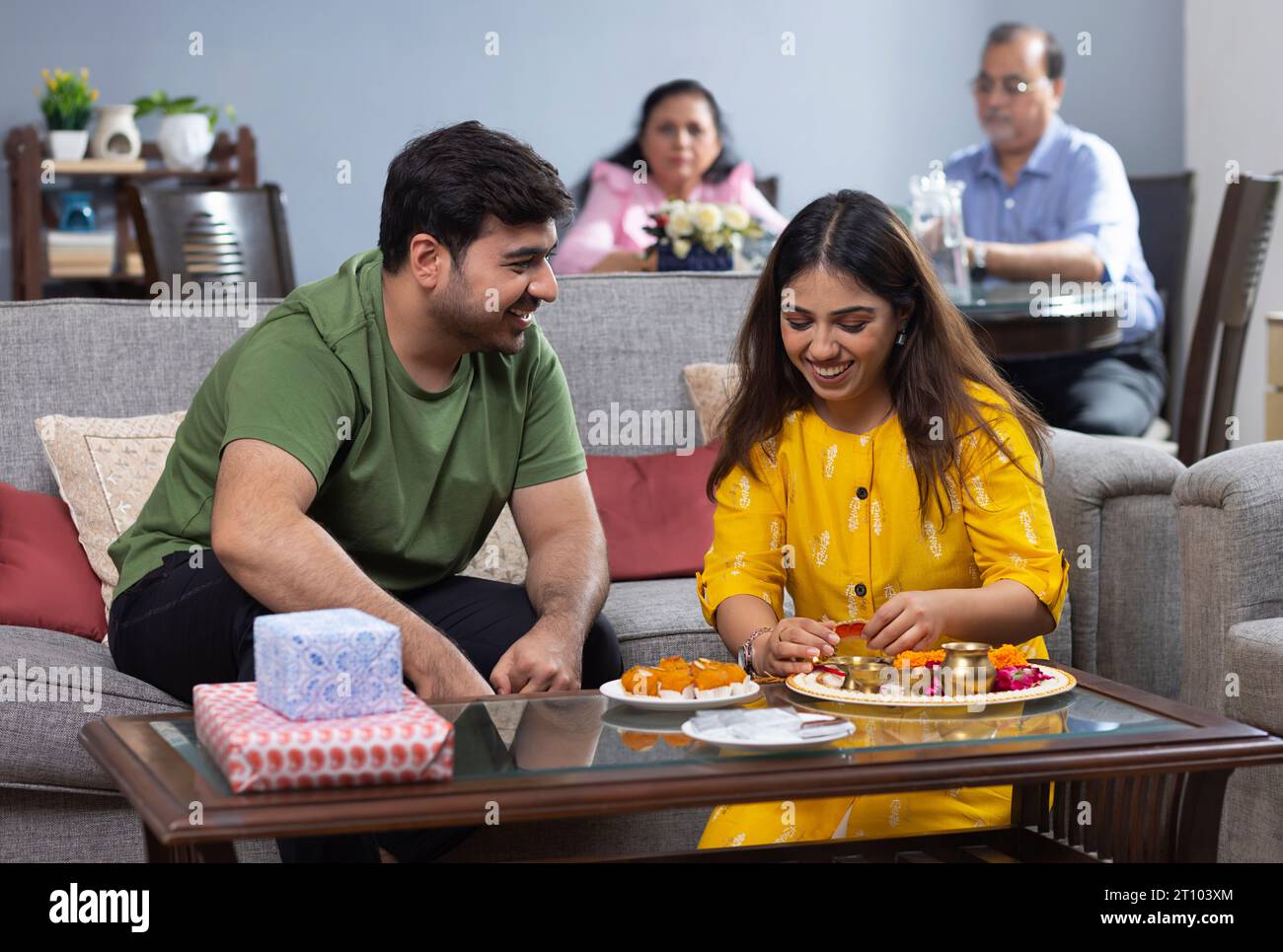 Geschwister feiern das Raksha Bandhan Festival zu Hause, während Eltern dahinter sitzen Stockfoto