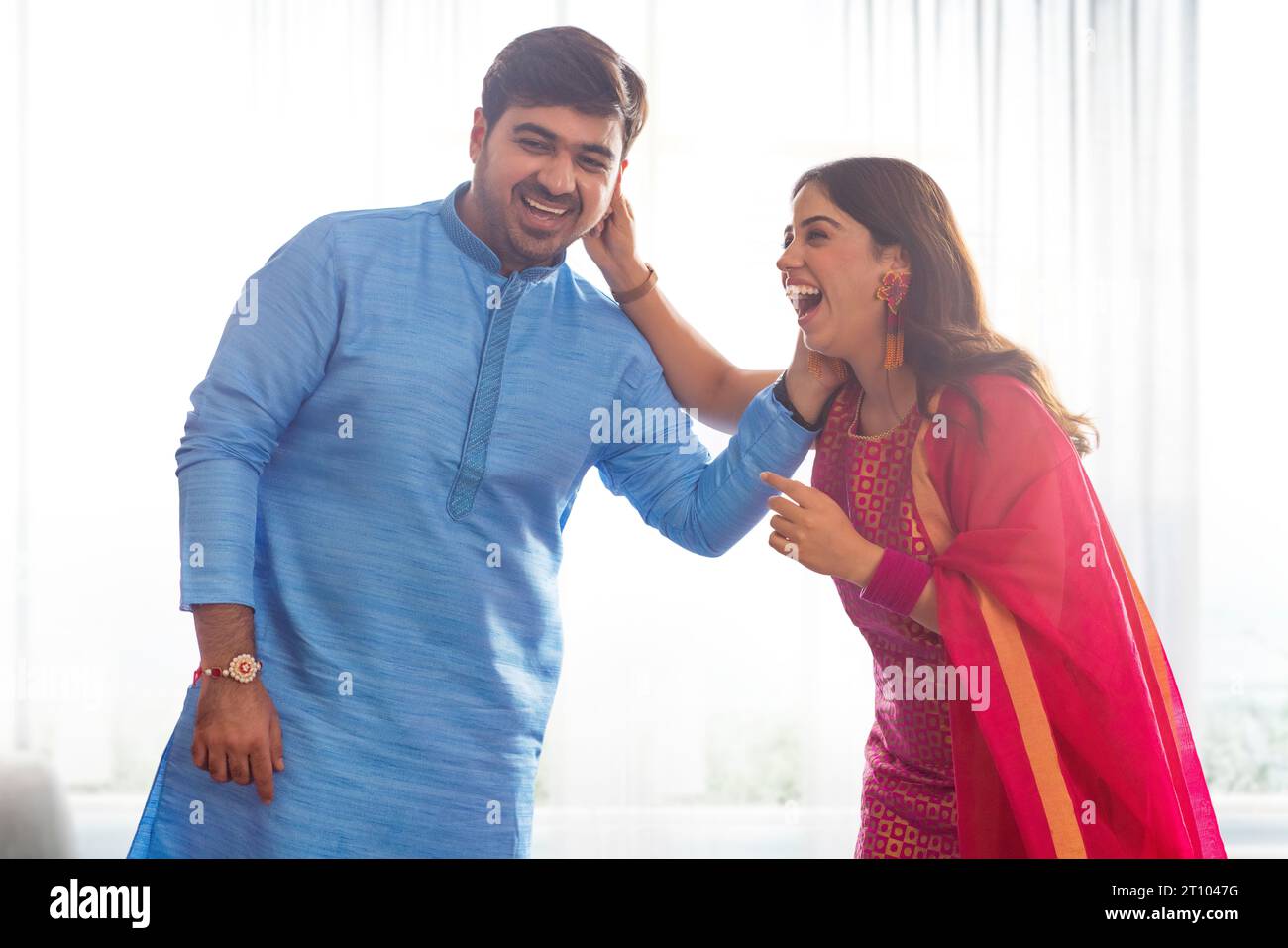 Geschwister ziehen sich liebevoll das Ohr, während sie Raksha Bandhan feiern Stockfoto