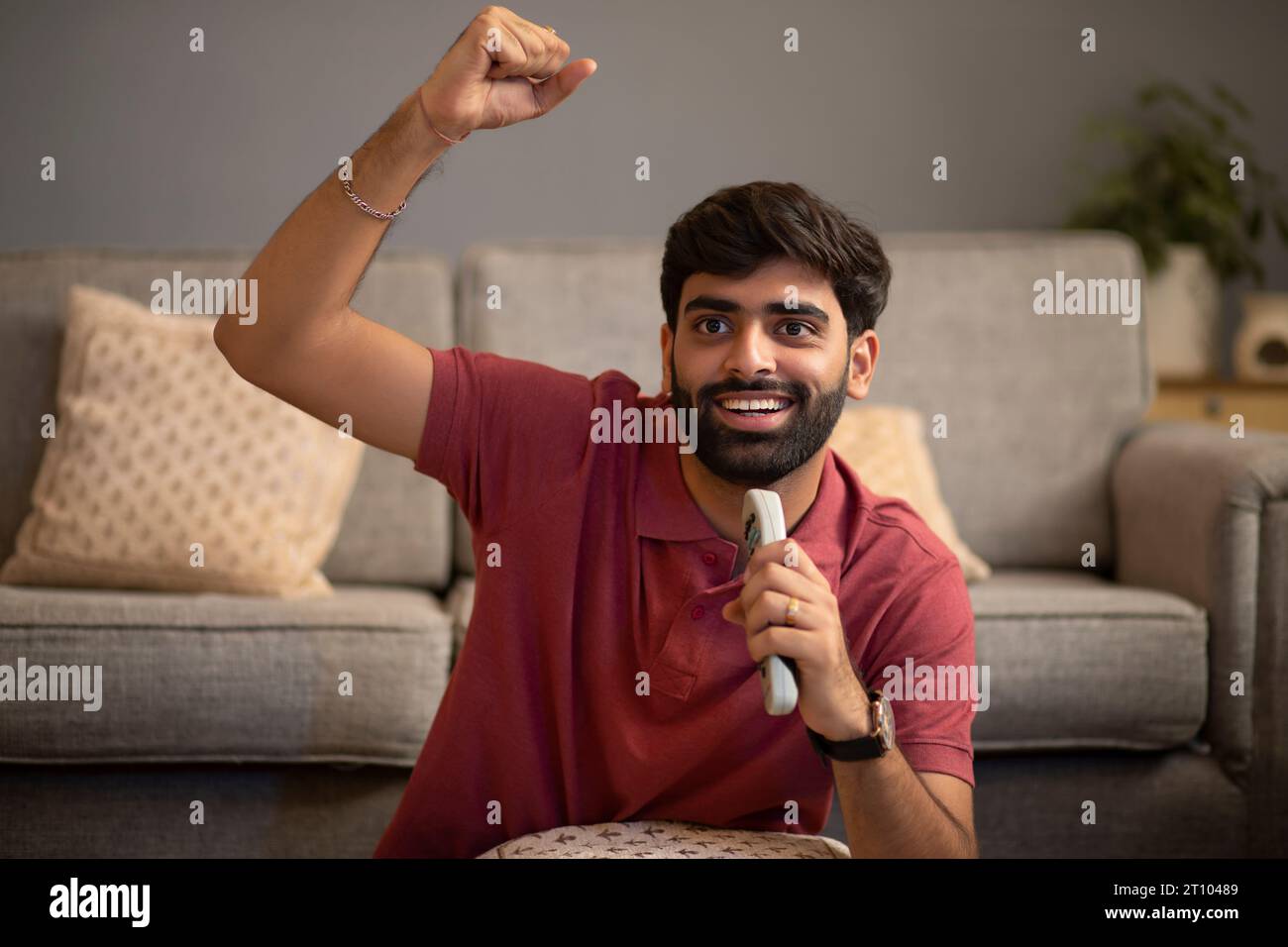 Porträt eines aufgeregten jungen Mannes, der beim Fernsehen im Wohnzimmer anfeuert Stockfoto