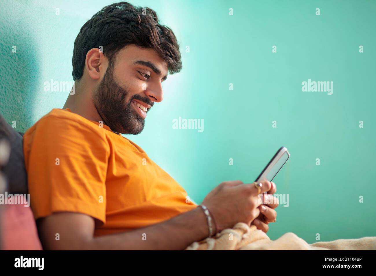 Junger Mann, der das Handy benutzt, während er sich im Bett entspannt Stockfoto