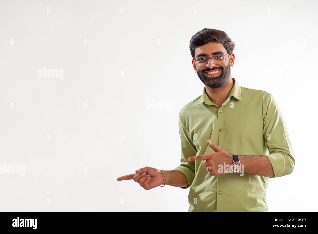 Porträt eines fröhlichen jungen Mannes, der seitwärts zeigt, während er vor weißem Hintergrund steht Stockfoto