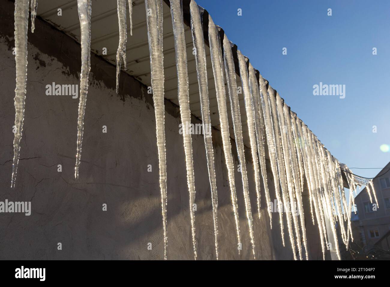 Scharfe Eiszapfen und geschmolzener Schnee hängen von Dachtrassen. Wunderschöne, transparente Eiszapfen, die langsam über ein Dach gleiten. Stockfoto