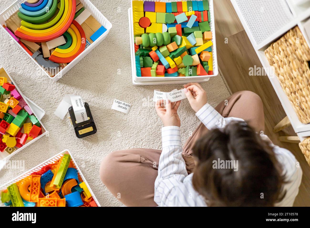 Frau reinigt kindliche Räume, sortiert Holz- und Plastikspielzeug, benutzt den Titel des mobilen Etikettendruckers Stockfoto