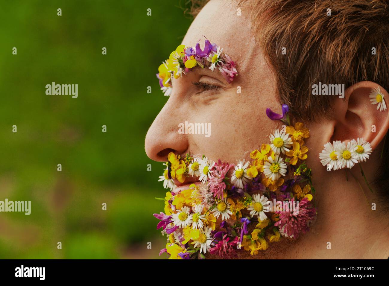 Umgeben von Bäumen sieht man einen Mann mit einem floralen Gesicht. Eine solche Affinität zur Natur, ob eingebildet oder real, spricht von seiner Leidenschaft für die Umwelt Stockfoto