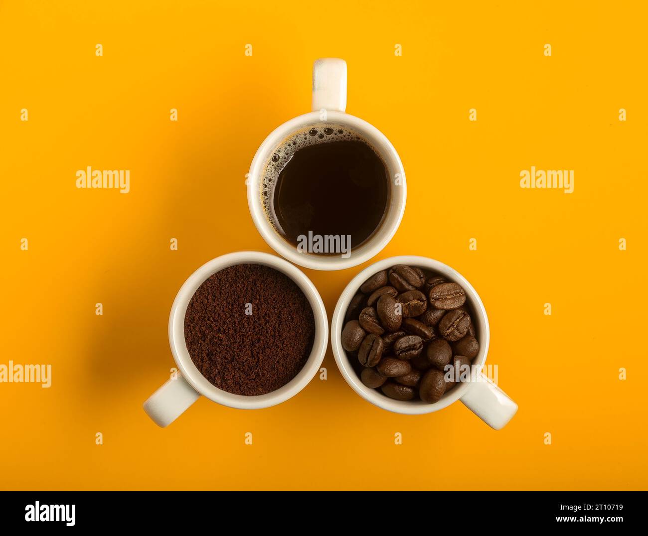 Blick von oben auf drei weiße Tassen Kaffee auf gelbem Hintergrund. Einer mit gemahlenem Kaffee, der andere mit Kaffeebohnen und der andere mit flüssigem Kaffee. Stockfoto