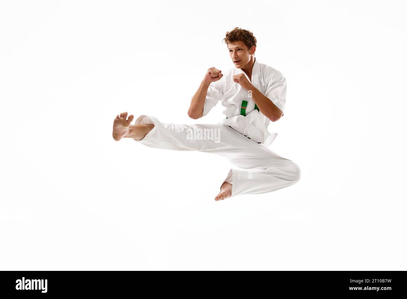 Junger sportlicher Mann, Karateka in weißem Kimono Training isoliert auf weißem Studio Hintergrund. Mann, der in Karate-Seitenttritt-Pose steht Stockfoto