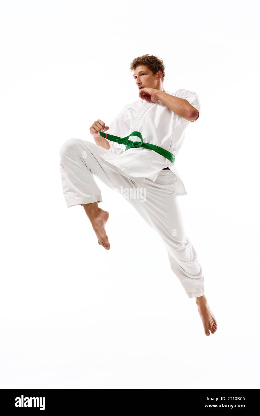 Sportlicher junger Mann, Karate, Taekwondo-Sportler in weißem Kimono in Bewegung, Training isoliert auf weißem Studiohintergrund Stockfoto