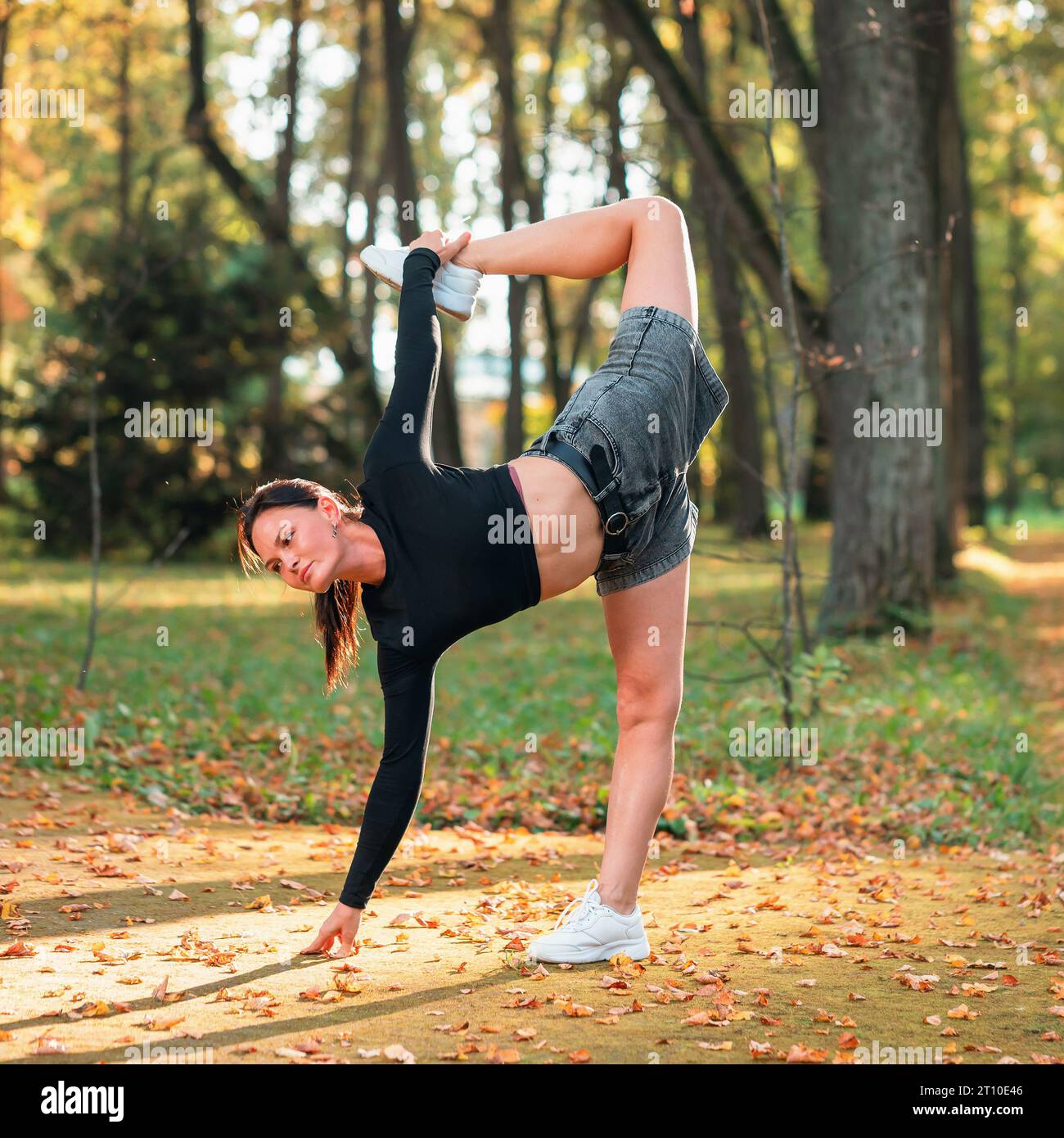 Eine Frau, die Yoga praktiziert, führt eine Variation der Ardha Chandrasana Übung durch, sichelförmige Haltung, Training, während sie an einem sonnigen warmen Herbsttag in t steht Stockfoto
