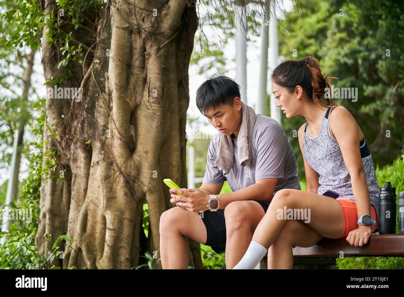 Junges asiatisches Paar teilt Handyfotos während einer Pause während des Trainings im Freien Stockfoto