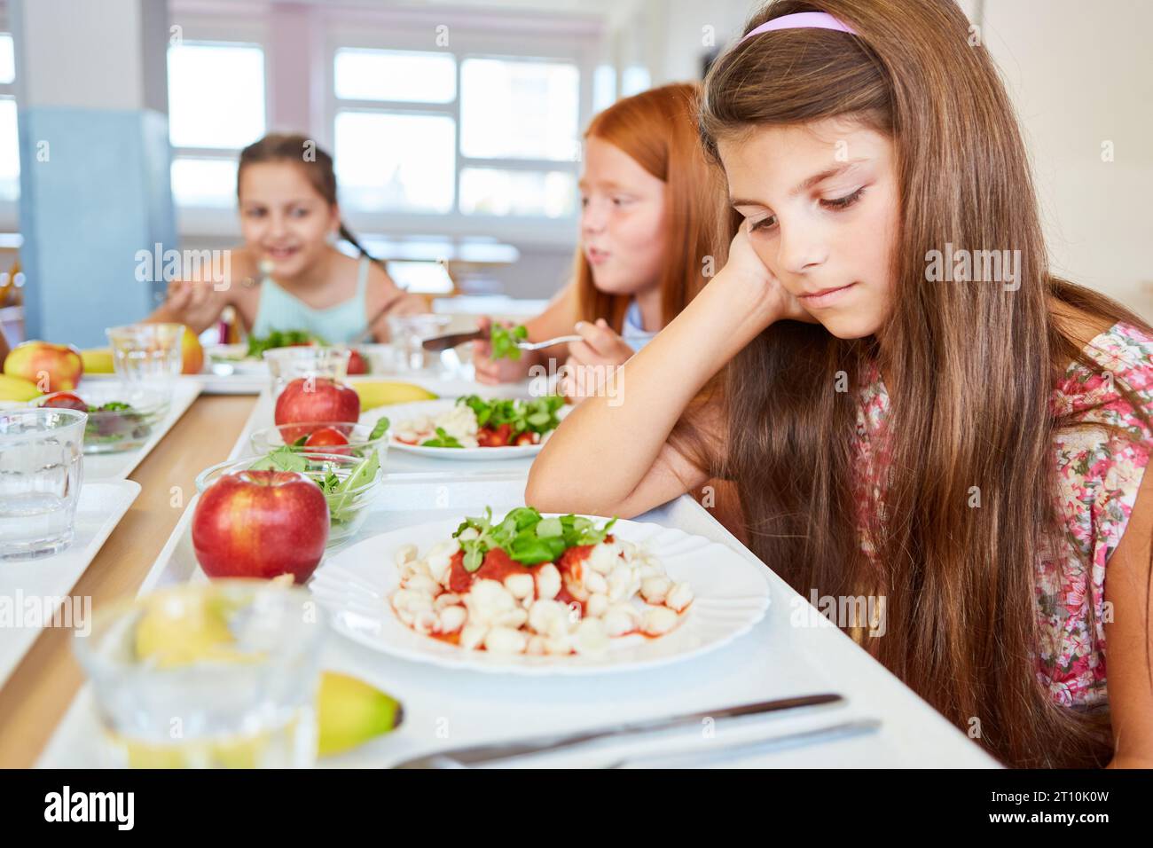Trauriges Mädchen, das sich auf den Ellenbogen stützt, während er auf die Essensplatte im Schulcafé starrt Stockfoto