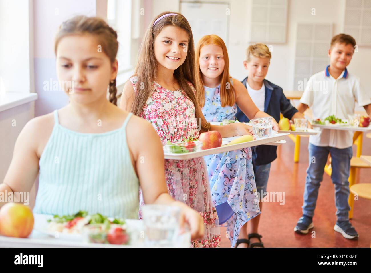 Porträt lächelnder Schülerinnen und Schüler mit Essensschalen, die während der Mittagspause in der Schulcafeteria anstehen Stockfoto