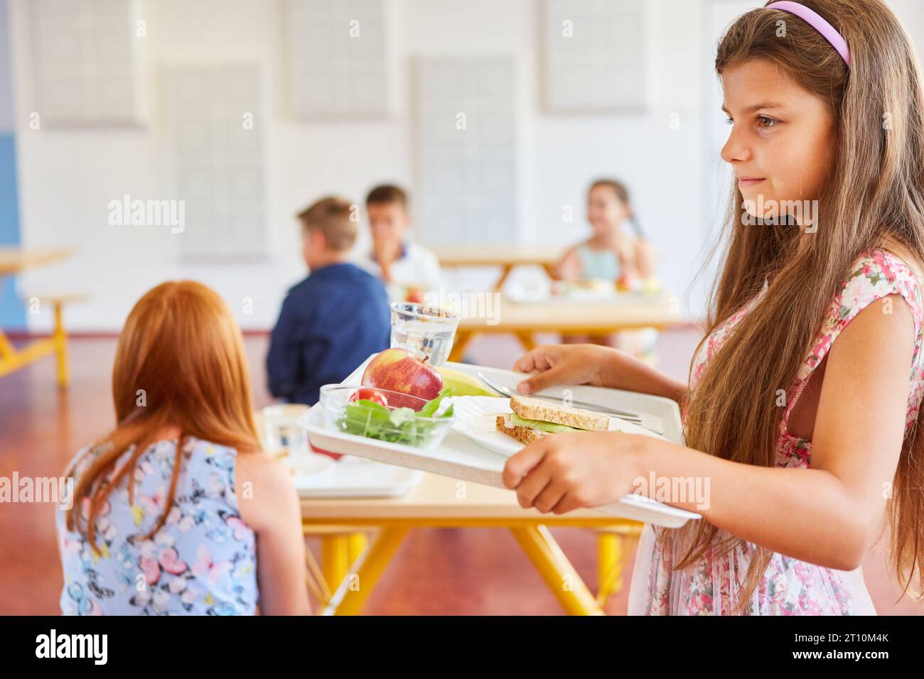 Seitenansicht eines Mädchens mit braunen Haaren, das in der Schulkantine eine Essensschale hält Stockfoto