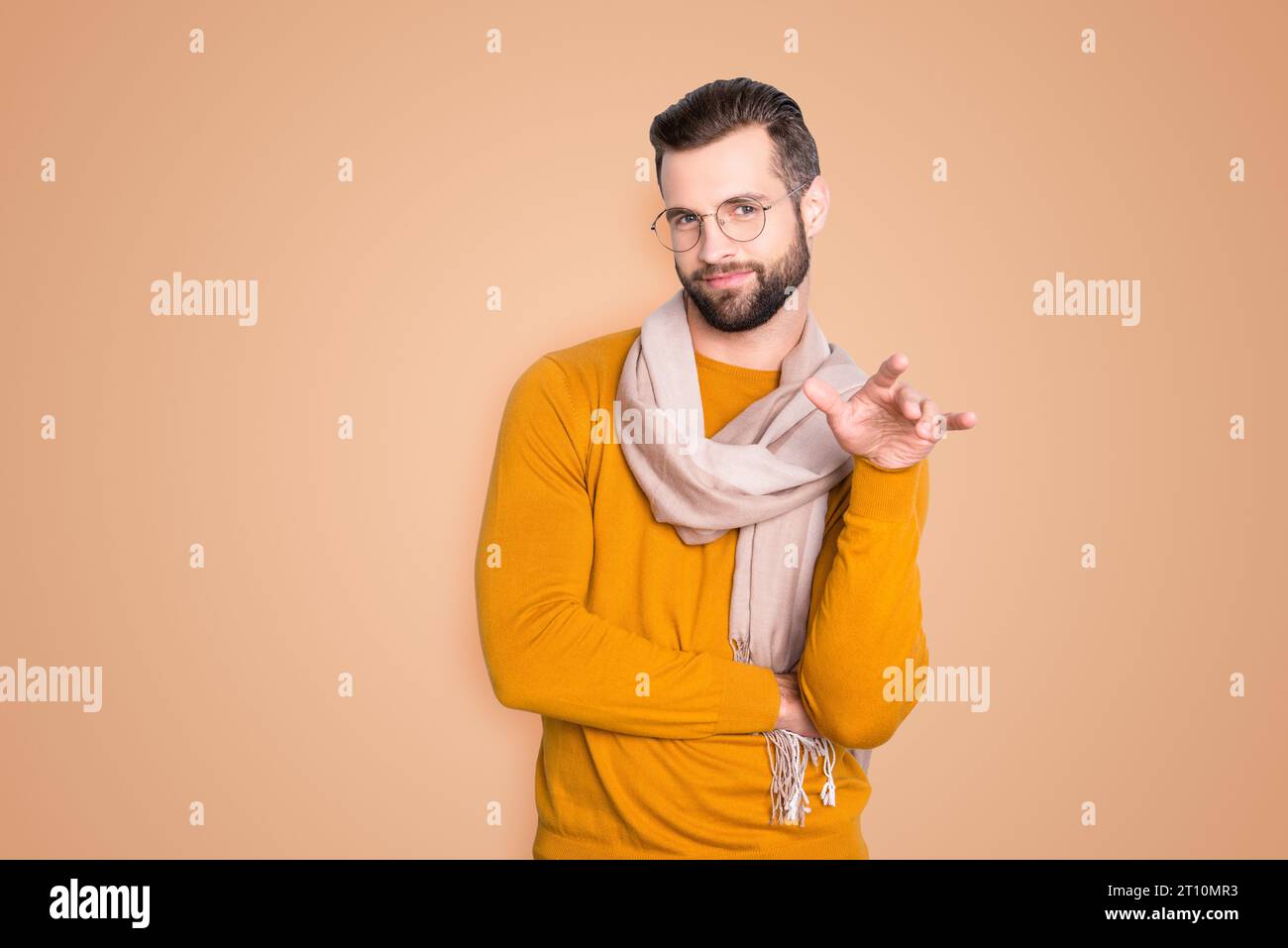 Porträt eines trendigen, stilvollen Stylisten in Brille, der Hand hält wie ein Schwuler, auf grauen Hintergrund isoliert auf die Kamera schaut und einen Schal um den Hals trägt Stockfoto