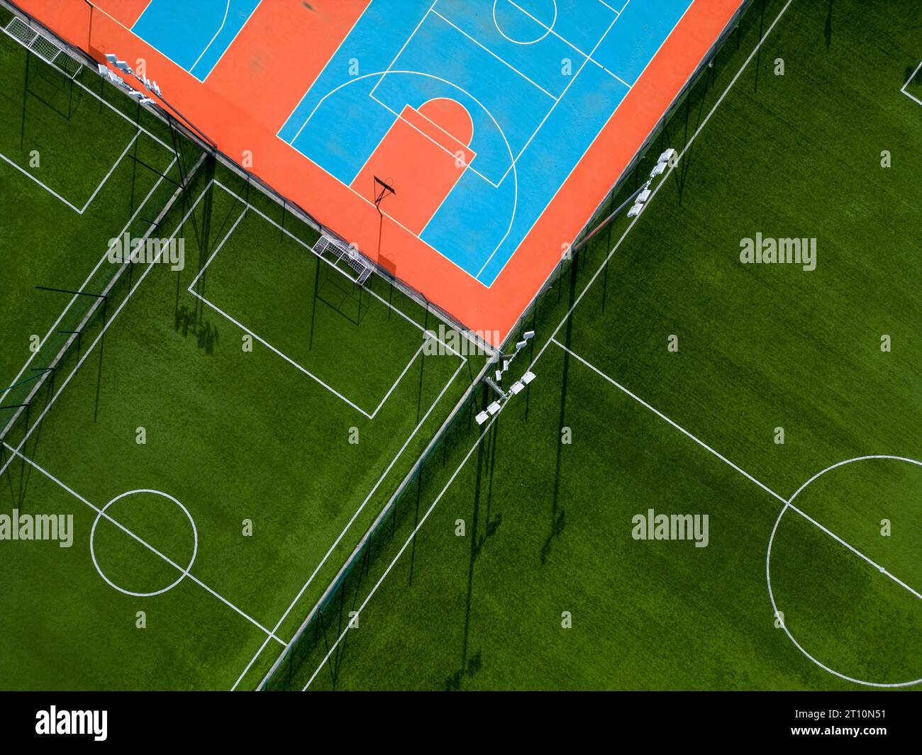 Aus der Vogelperspektive auf ein grünes Fußballfeld und einen farbenfrohen Basketballplatz, der einen Blick auf zwei verschiedene Sporteinrichtungen nebeneinander bietet. Das Gegenteil Stockfoto