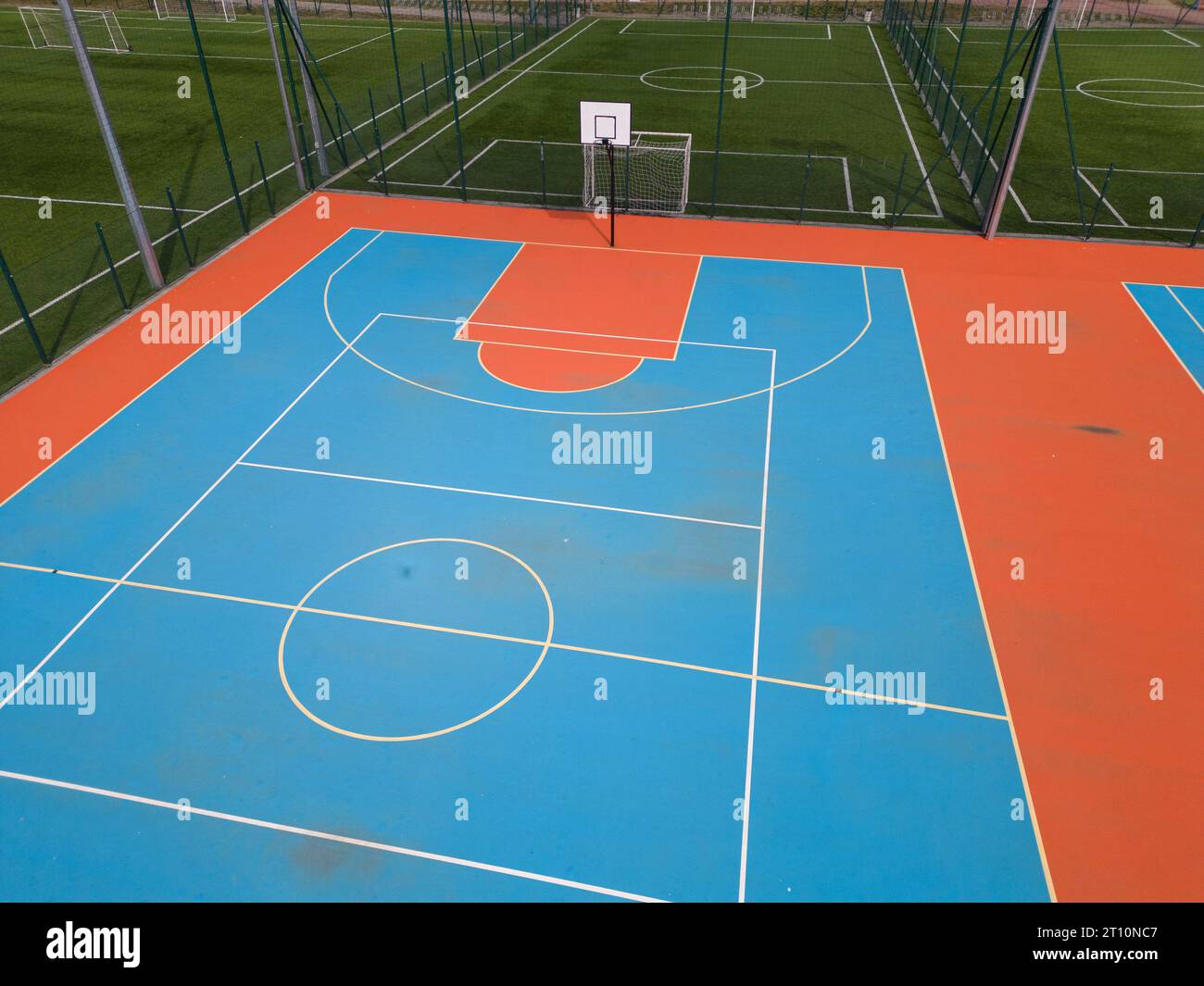 Aus der Vogelperspektive auf ein grünes Fußballfeld und einen farbenfrohen Basketballplatz, der einen Blick auf zwei verschiedene Sporteinrichtungen nebeneinander bietet. Das Gegenteil Stockfoto