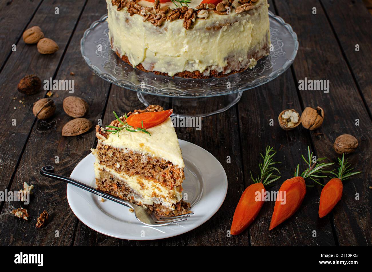 Karottenkuchen mit Walnüssen auf dunklem hölzernem Hintergrund. Selektiver Fokus. Ein Stück Kuchen in einer Schüssel und Walnüsse und Karotten. Stockfoto