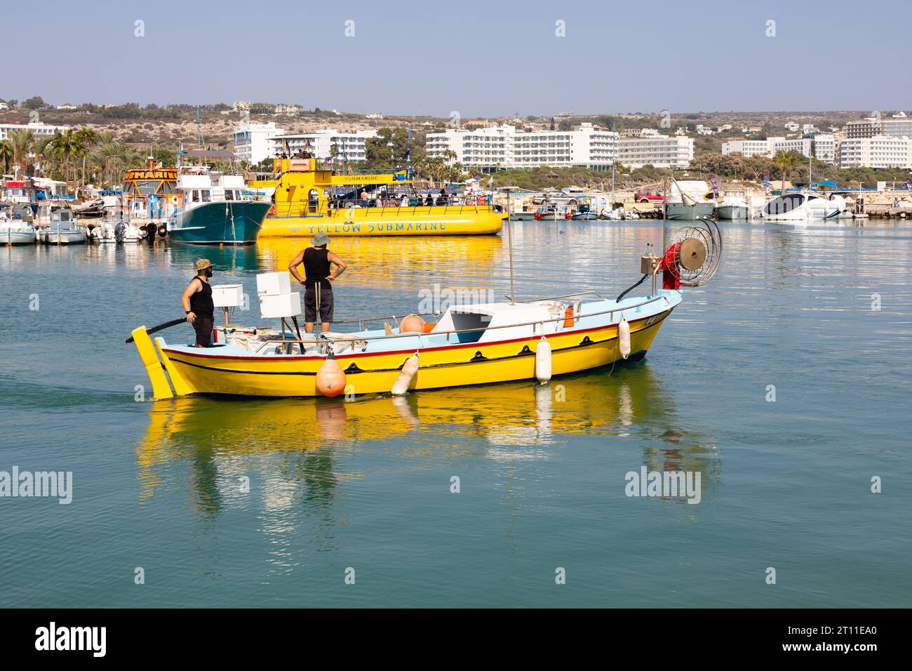 Fischer starten vom Hafen Ayia Napa in einem hellgelben, traditionellen zyprischen Fischerboot mit dem gelben U-Boot dahinter. . Ayia Napa, Zypern Stockfoto