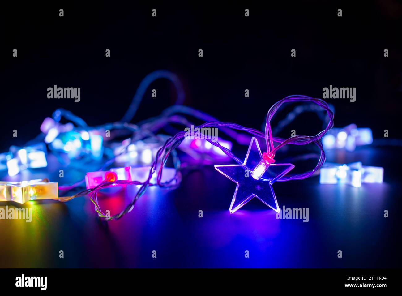 Nahaufnahme von rosa und lila elektrischen weihnachtsschnur Lichtergirlande in Form von Sternen, modernes Ferienhaus Dekor auf schwarzem Hintergrund Stockfoto