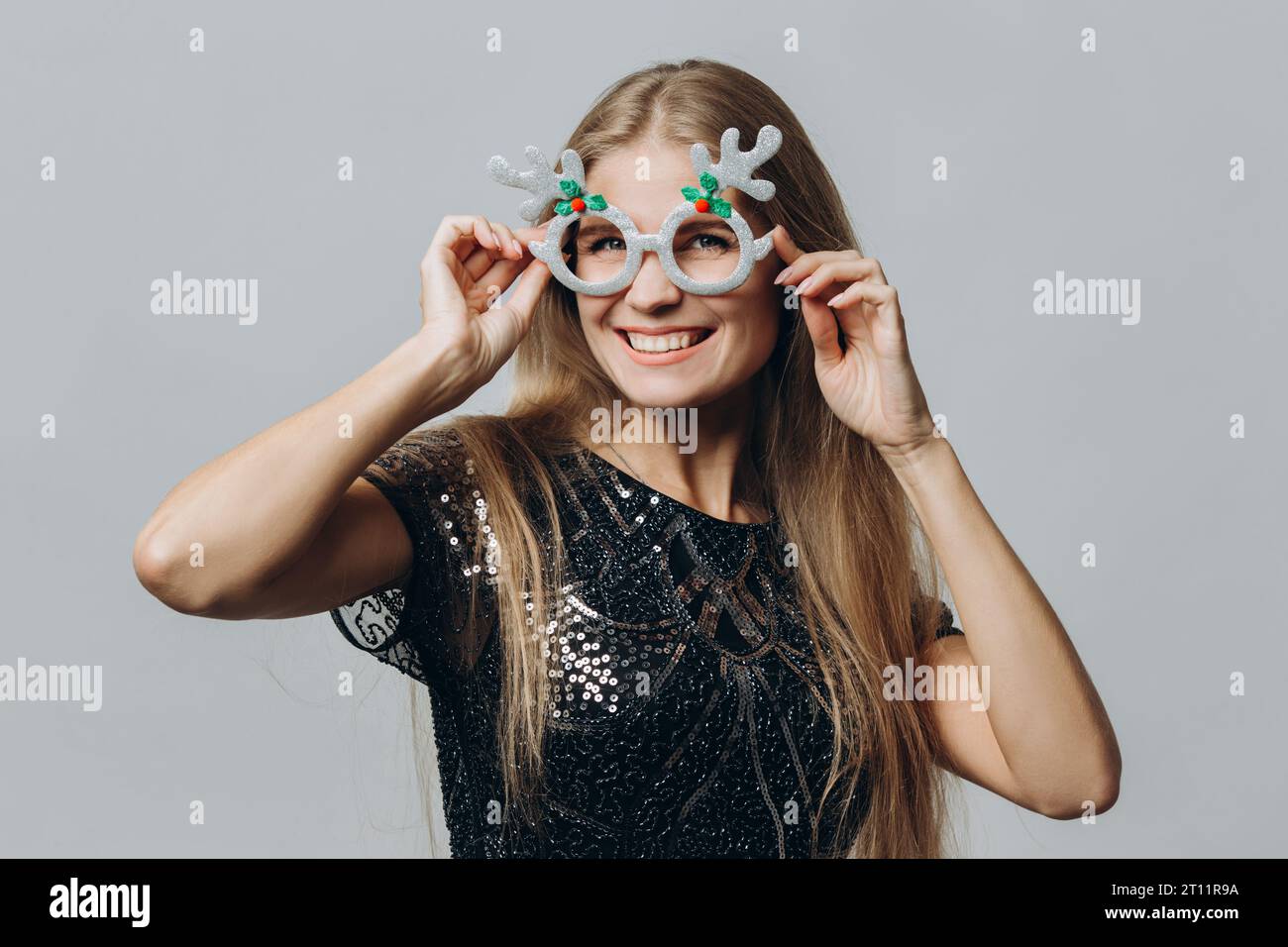 Eine junge lächelnde blonde Frau in Brille mit Hirschgeweih isoliert auf weißem Hintergrund. Weihnachts- und Neujahrskonzept. Stockfoto