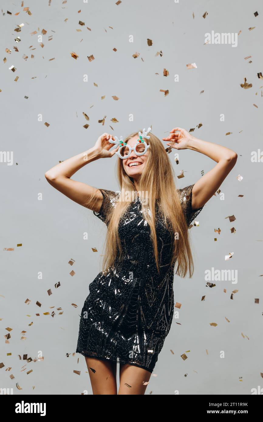 Ein hübsches blondes Mädchen tanzt unter glitzerndem Konfetti. Neujahrsfest-Konzept. Stockfoto